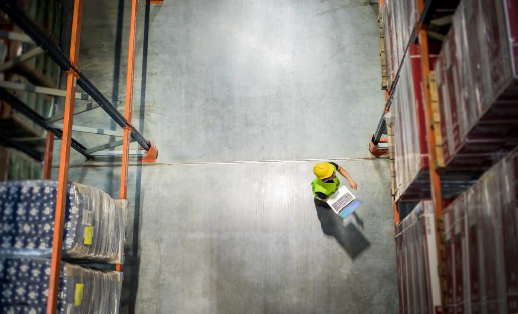 A warehouse aisle seen from above, with a worker holding a laptop
